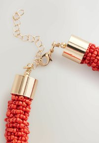 Collar de cuentas rojas con cierres y cadenas de tono dorado, destacando un acabado texturizado y brillante, así como una intrincada disposición de las cuentas.