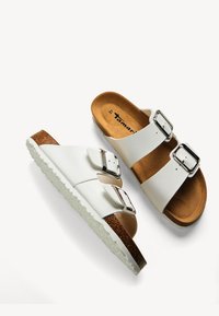 White two-strap sandals with silver buckles, cork footbed, and a textured white outsole. Brown bottom accent and soft inner lining.