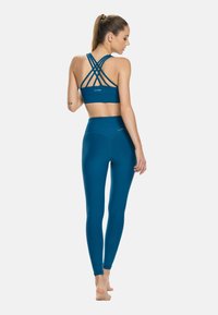 Sostén deportivo verde azulado con tirantes en la espalda cruzados, combinado con leggings de cintura alta en el mismo tono. Textura suave y diseño ajustado.