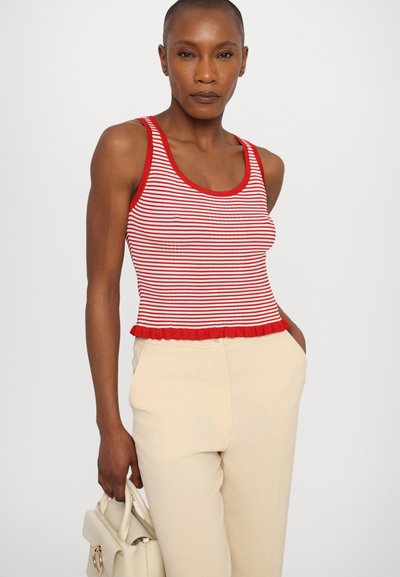 Débardeur à rayures rouge et blanc avec un col rond et un ourlet volanté, associé à un pantalon beige clair et tenant un sac à main couleur crème.