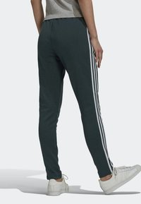 Mörkgröna sweatpants med en figurnära design, med vita sidostrecker. Tillverkade av mjukt material med en slät yta. Matchat med vita sneakers.
