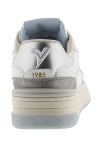 Sneaker bianco con un tallone metallico argento lucido, interno azzurro e dettaglio dorato "1985". Presenta una suola grigia testurizzata e una intersuola a strati.