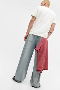 Løse, lyseblå cowboybukser kombineret med en hvid T-shirt. En rødternet skjorte er lagt over taljen. Flade sorte sko er synlige.