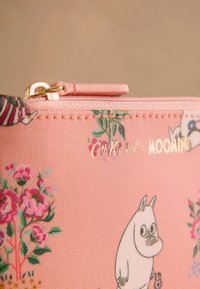 Rožinė tekstūruota audinio rankinė su gėlių raštais, Moomin personažo iliustracija ir auksinėmis raidėmis "Cath Kidston x Moomin". Auksinė užtrauktuko sistema.