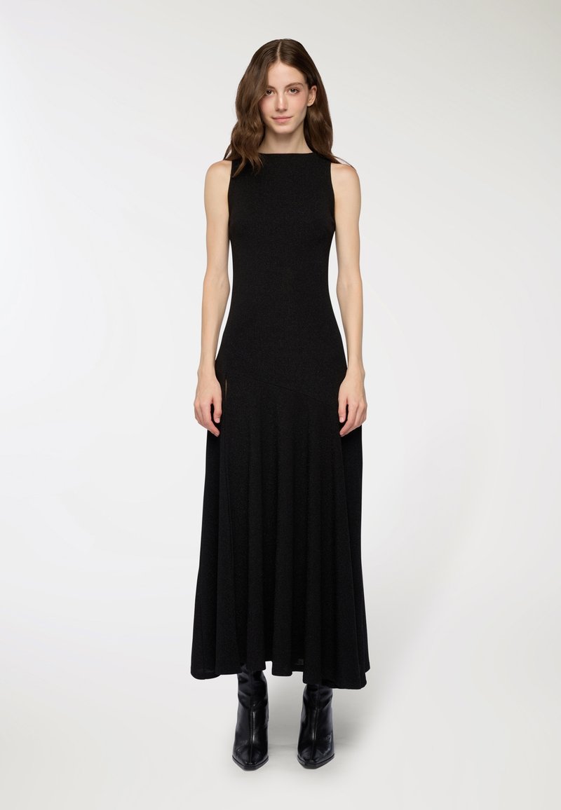 Abito maxi nero senza maniche con corsetto aderente e gonna ampia. Tessuto liscio, design minimalista, abbinato a stivali neri con punta.