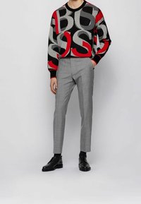 Svart, röd och grå mönstrad stickad tröja i kombination med skräddarsydda grå byxor, vilket fulländar looken med svarta läderskor.