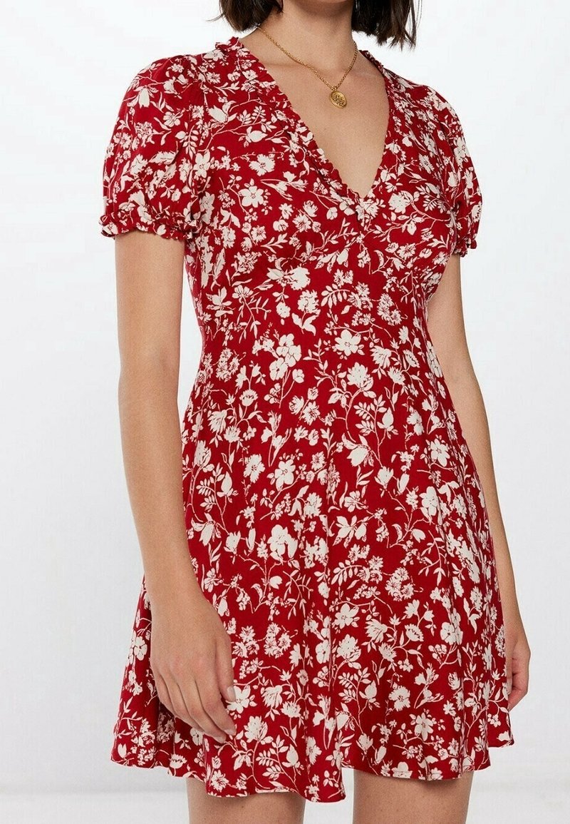 Rotes Blumenkleid mit kurzen, puffartigen Ärmeln und V-Ausschnitt. Verfügt über weiße Blumenmuster, einen ausgestellten Rock und leichten Stoff.