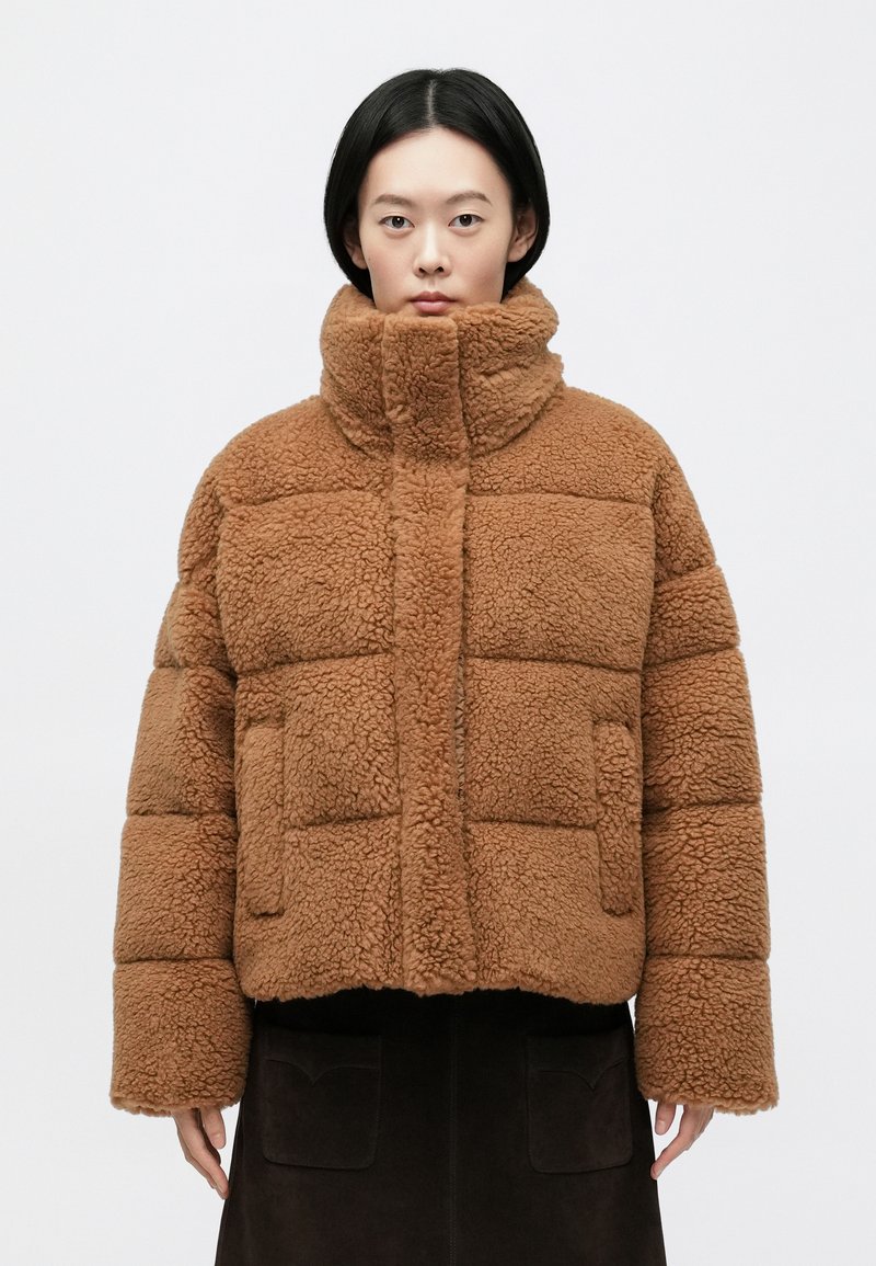 Brązowa, pluszowa, krótka puchowa kurtka z wysokim kołnierzem, pikowanym wzorem i przednimi kieszeniami, wykonana z miękkiego, teksturowanego materiału.