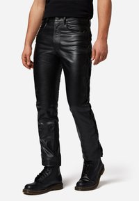 Zwarte leren broeken met een slim fit, voorzien van gevlochten accenten langs de zijkanten en meerdere zakken. Het materiaal heeft een glanzende afwerking.