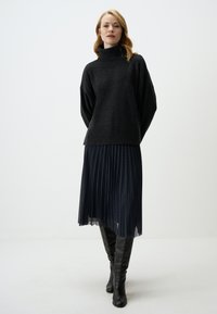 Schwarzer Rollkragenpullover mit weiten Ärmeln, kombiniert mit einem geglätteten schwarzen Rock mit strukturiertem Muster, abgerundet durch knielange schwarze Stiefel.