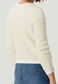 Cremfarbener Pullover aus weichem, strukturiertem Stoff, mit langen Ärmeln und einem gerippten weißen Saum, kombiniert mit einem Denimrock.
