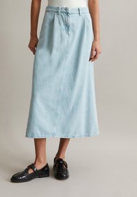 Ljusblå denimkjol med en avslappnad passform, knälång, med midjeband, bälteshällor och sidofickor. Matchas med svarta skor.