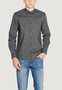Camicia a righe bianco e nero con colletto a camicia, maniche lunghe, vestibilità slim e una texture liscia, abbinata a jeans azzurri chiari.