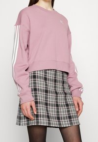 Rosa kort hoodie med vita ränder på ärmarna, ihopparad med en svart och vit rutig minikjol. Slät textur, avslappnad passform.