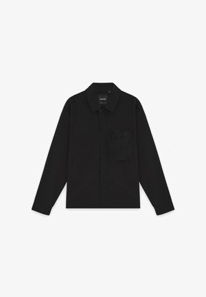 Svart langermet skjorte med knapper, krage og en glidelåslomme på venstre bryst, lagt flatt på en hvit bakgrunn.