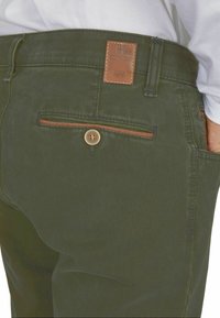 Ciemnozielone męskie spodnie uszyte z mieszanki bawełny. Posiadają skórzaną naszywkę, zapięcie na guzik oraz detalowane przeszycia kieszeni.