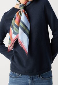 Foulard di seta con strisce multicolori di larghezze variabili, annodato al collo, indossato sopra un maglione blu navy, aggiungendo un contrasto vivace.