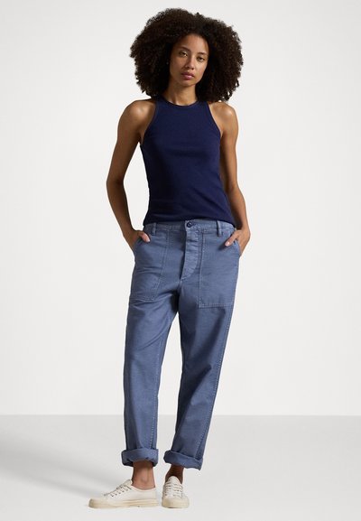 Canotta a costine blu navy abbinata a pantaloni chiari, dal taglio morbido, con tasche frontali e risvolti, indossati con sneakers color crema.