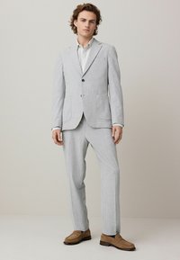 Traje gris claro con estampado, compuesto por una chaqueta de un botón y pantalones rectos, combinado con una camisa clara y mocasines marrones.