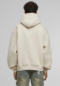 Beige oversized hættetrøje med en stor hætte, ribbede manchetter og en ensfarvet ryg. Blød tekstur, afslappet design, egnet til lagdeling over andre beklædningsgenstande.
