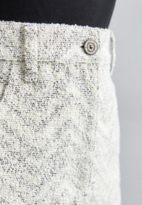 Kareda heledad helehalli kangas püksid, millel on sik-sak muster, ees nupuga kinnitamine ja vöödetailid.