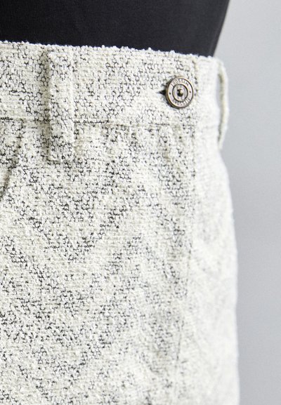 Pantalon en tissu gris clair texturé avec un motif en zigzag, un bouton à l'avant et des détails au niveau de la taille.
