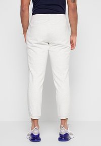 Hellgraue Jogginghose mit elastischem Bund, schmal zulaufendem Bein und seitlichen Taschen. Kombiniert mit weißen und grauen Sneakers mit violetten Akzenten.