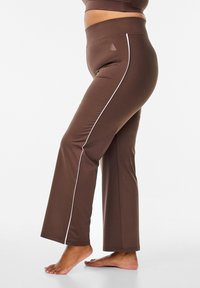 Brown flared pants in a stretchy material with a high waistband and white side piping. Features an elastic waistband for comfort.
