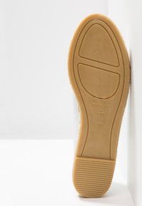 Semelle d'une chaussure beige avec talon texturé, taille 37, marquée "Made in Spain", positionnée verticalement sur un fond blanc avec coins.