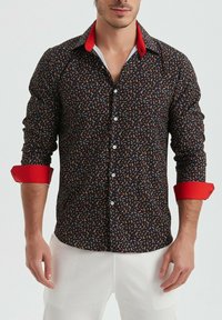 Chemise noire à boutons avec un motif paisley coloré ; col et poignets rouges ; manches longues, design ajusté et texture lisse.