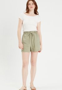 White ribbed T-shirt paired with light olive green linen shorts featuring an elastic waistband and drawstring. Simple sandals complete the look.