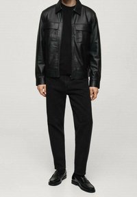 Chaqueta de cuero negro con dos bolsillos frontales, combinada con un suéter negro, jeans oscuros y mocasines negros. Textura suave y cierre con cremallera.