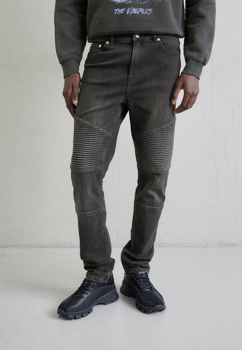 Faded black denim jeans with ribbed panel accents on knees, five-pocket design, and metal hardware at the waist for closure.