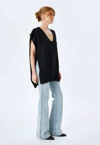 Top de punto negro sin mangas con escote en V y aberturas laterales, combinado con jeans acampanados de un azul claro y tacones negros de punta. Ajuste simple y relajado.