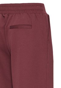 Pantaloni de trening burgund cu un talie elastică, țesătură texturată și un buzunar discret pe spate. Design simplu, conic. Fără detalii suplimentare.