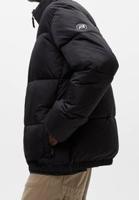 Veste matelassée noire avec fermeture éclair, design oversize, ourlet élastique et poches latérales. Comprend un logo sur le haut du bras.