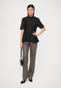 Svart peplum topp med korte ermer, kombinert med brune skinnbukser. Modellen holder en liten svart håndveske og har på seg svarte spisse hæler.