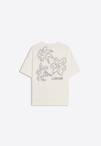 T-shirt manches courtes couleur crème avec trois grandes fleurs tropicales noires en contour et le texte "Hidden Days" dans le dos.