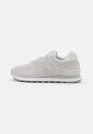 Baskets New Balance gris clair en tissu texturé, semelle blanche, et fermeture à lacets, vues de côté gauche sur un fond uni.