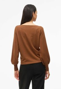 Pull en maille marron avec une coupe décontractée, un large col bateau, des manches longues bouffantes et des poignets côtelés, associé à un pantalon noir.