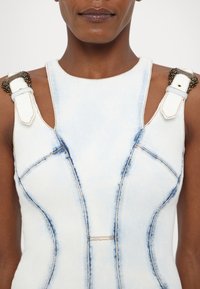 Light blue denim jumpsuit with structured design, featuring gold-toned hardware on the shoulder straps and contrasting stitching details.