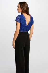 Top in pizzo blu con maniche corte e schiena a V ondulata, abbinato a pantaloni neri a vita alta in un tessuto morbido.