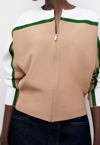 Giacca beige con zip e strisce bianche e verdi sulle spalle. Tessuto morbido, design aderente, finitura testurizzata e scollo alto.