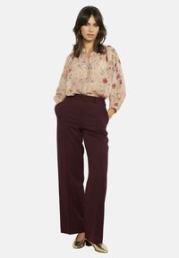 Blūze ar ziedu rakstu gaiši rozā krāsā, kopā ar augsta vidukļa bordo platām biksēm. Apģērbu papildina zelta metāliskas kurpes.