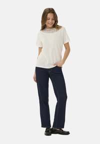 T-shirt bianca con un dettagliato colletto in pizzo, maniche corte, abbinata a jeans blu scuro a gamba dritta e scarpe nere.