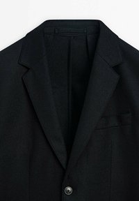 Blazer noir ajusté avec revers crantés, fermeture par un seul bouton et une poche poitrine passepoilée, réalisé dans un tissu doux et structuré.