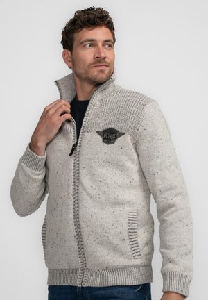 Cardigan en maille gris clair avec un col montant, tissu texturé, fermeture éclair, poches latérales et un patch logo noir sur la poitrine.