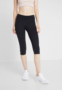 Leggings capri noirs en tissu extensible, dotés d'une taille lisse et d'une coupe ajustée, associés à des chaussures de sport blanches.