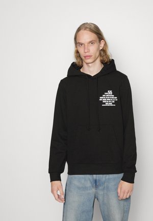 Zwarte hoodie met een voorzak, capuchon met trekkoord en witte tekstdetails op de linkerkant van de borst; zachte stof met een losse pasvorm.