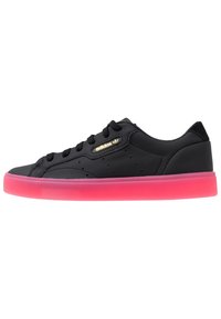 Black leather sneakers with a textured surface, featuring a pink translucent sole and gold branded accents. Lace-up design with ventilation holes.
